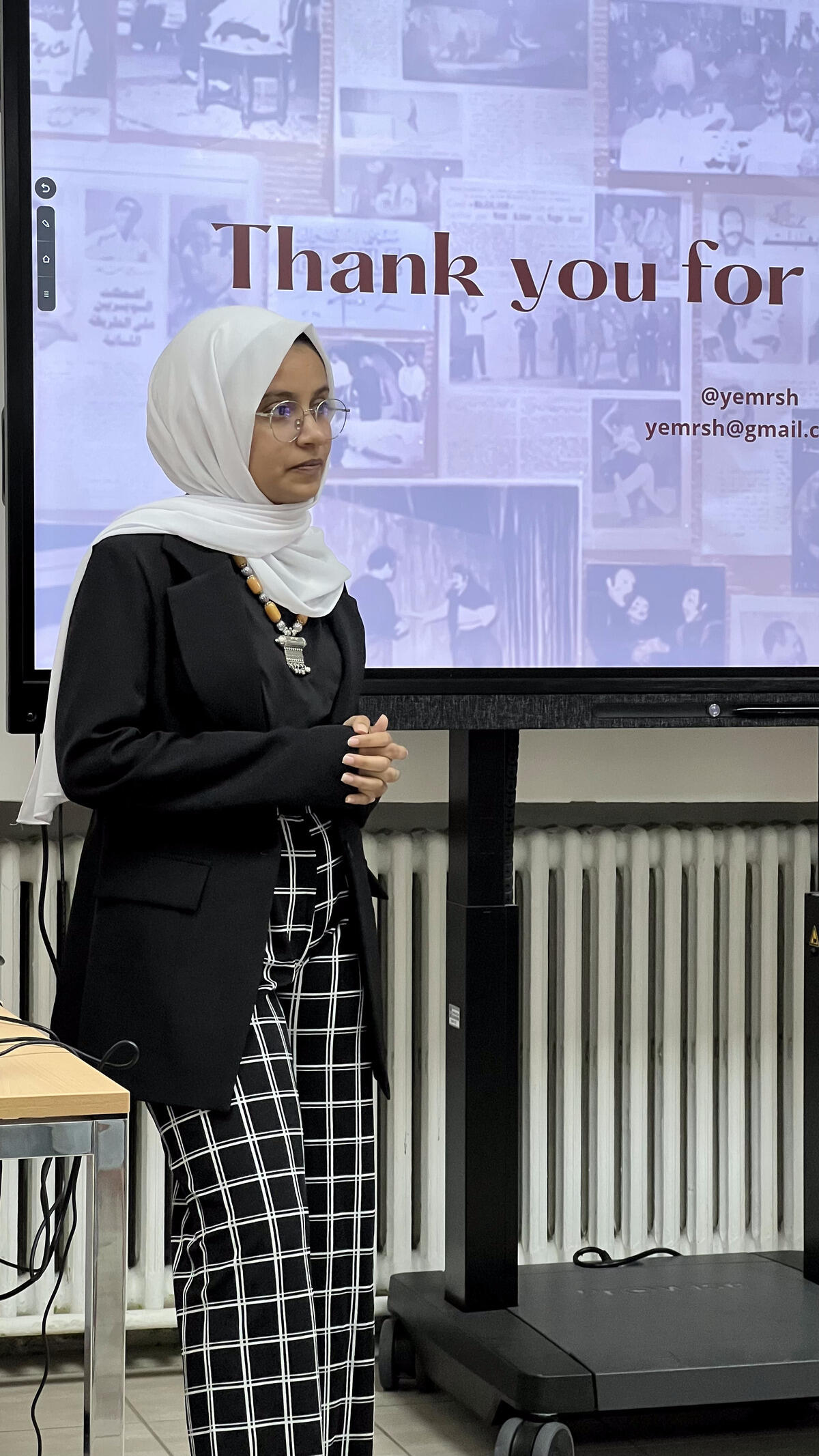 A photo of a woman standing in front of a screen that says \"Thank you for\" 