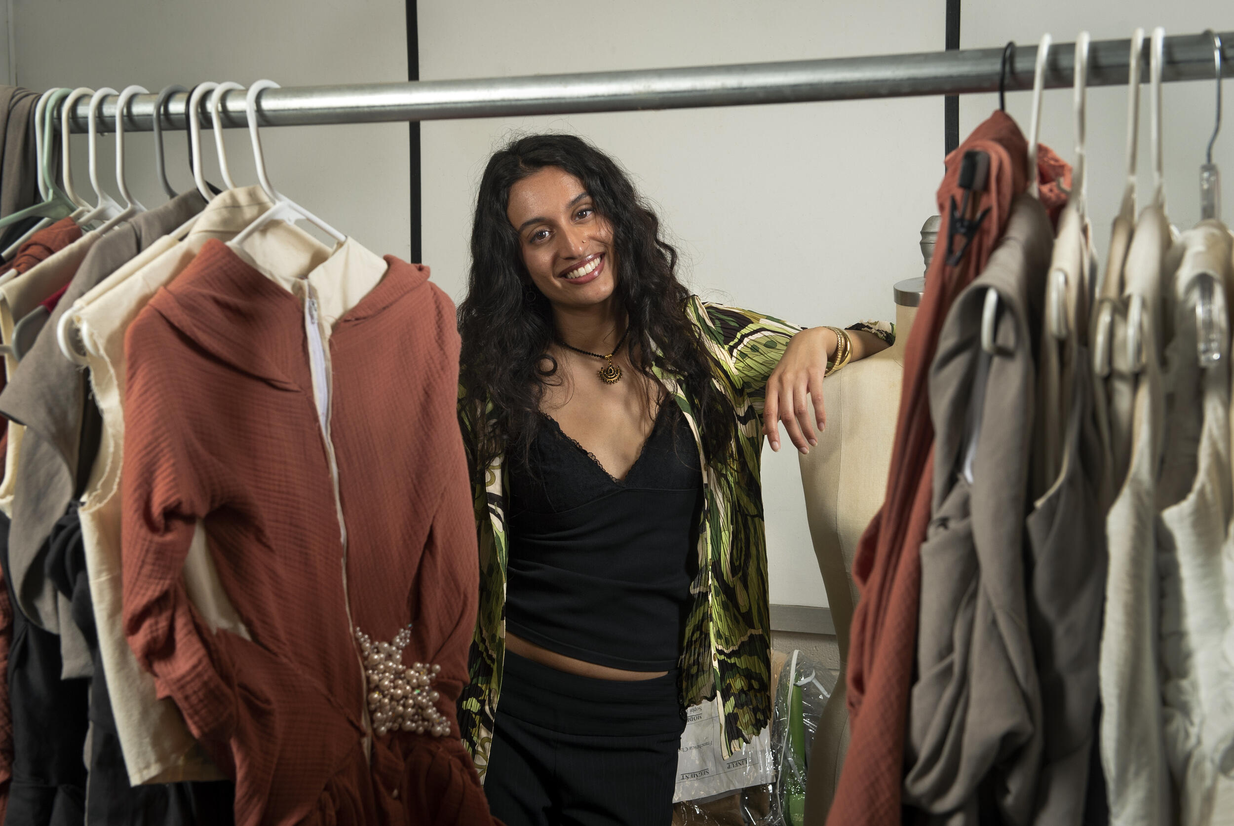 A photo of a woman standing behind a rack of clothes 