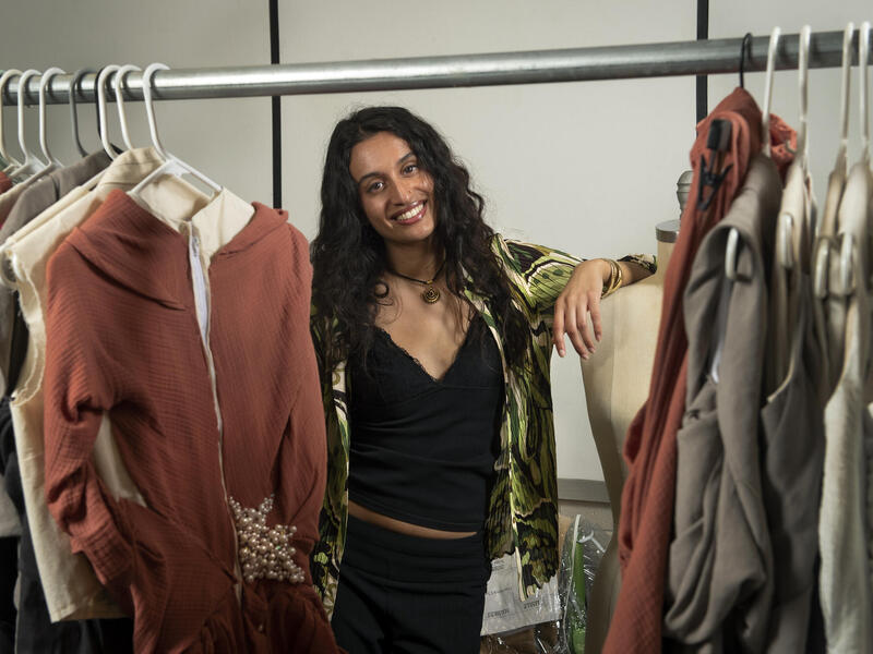 A photo of a woman standing behind a rack of clothes 