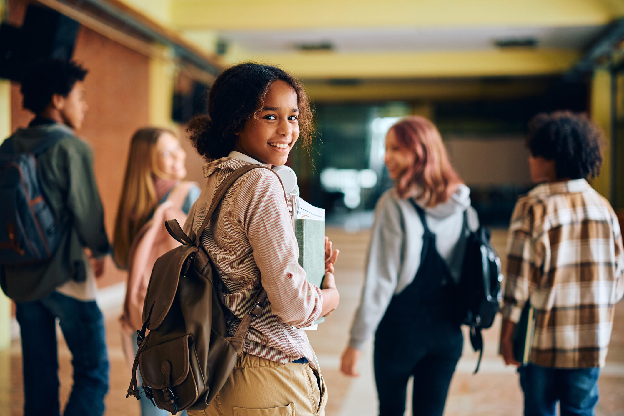An photo of Black and white children walking down a hallway. A Black girl looks behind her smiling. 