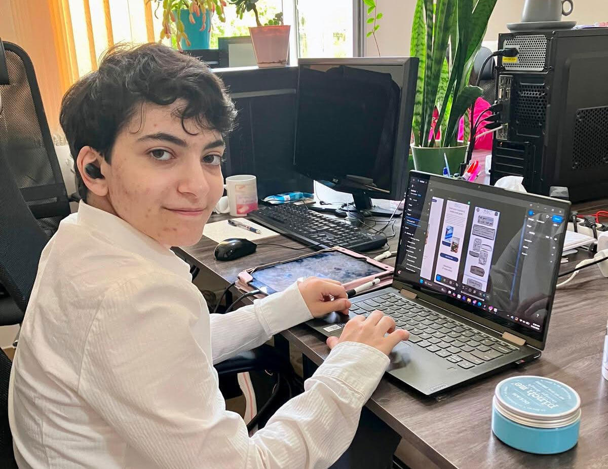 A photo of a man sitting at a table with a laptop. 