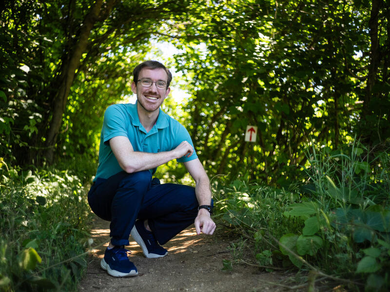 A photo of a man kneeling on a path in the woods. 