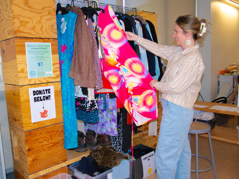 A photo of a woman pulling a dress from a rack and looking at it. 