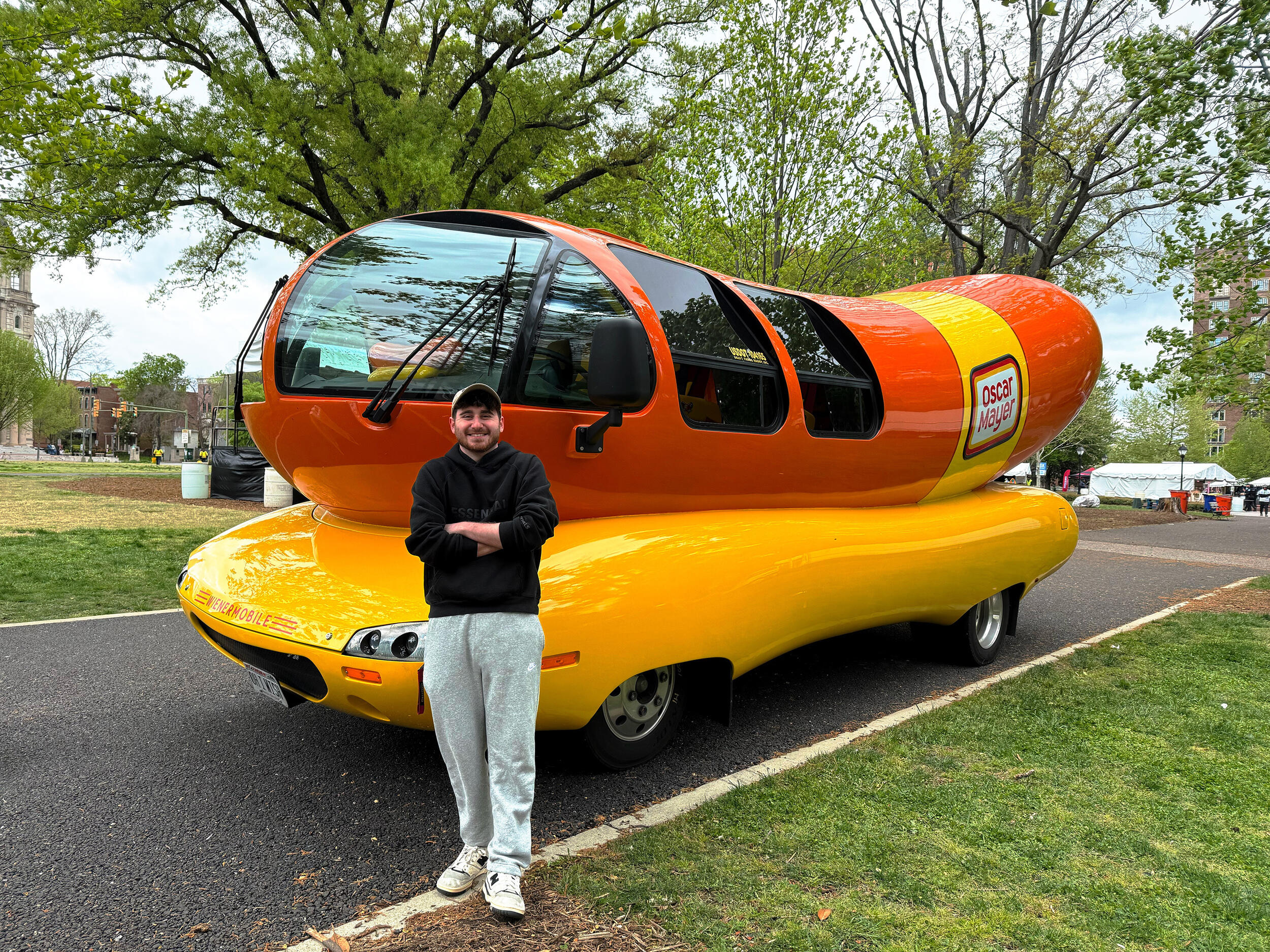 A photo of a man standing in front of a car that is shaped like a hot dog. 