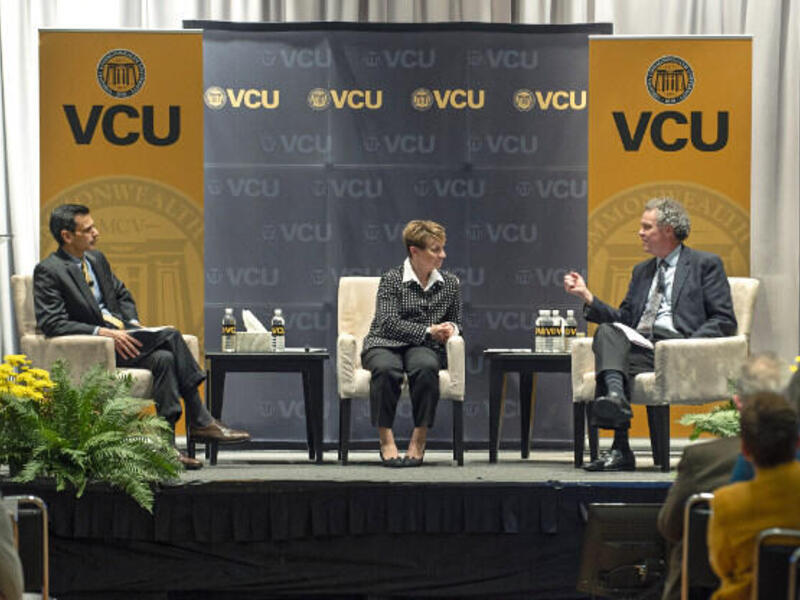 Three people sit in chairs under banners reading VCU.