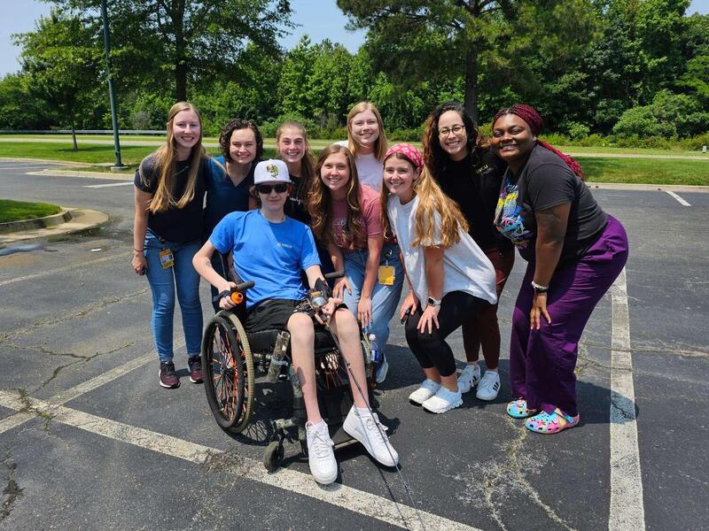A man in a wheelchair poses with a group of women standing around him.