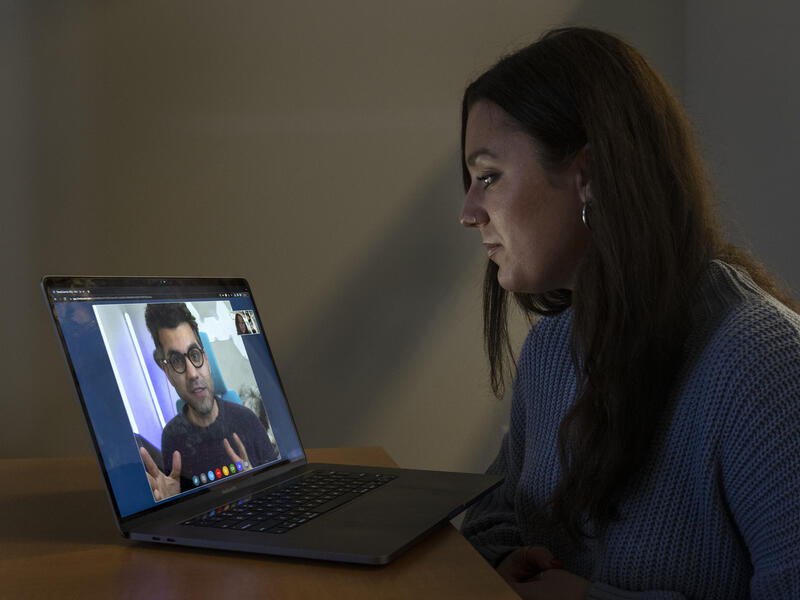 A student looks at a laptop screen, where a mental health provider is speaking.