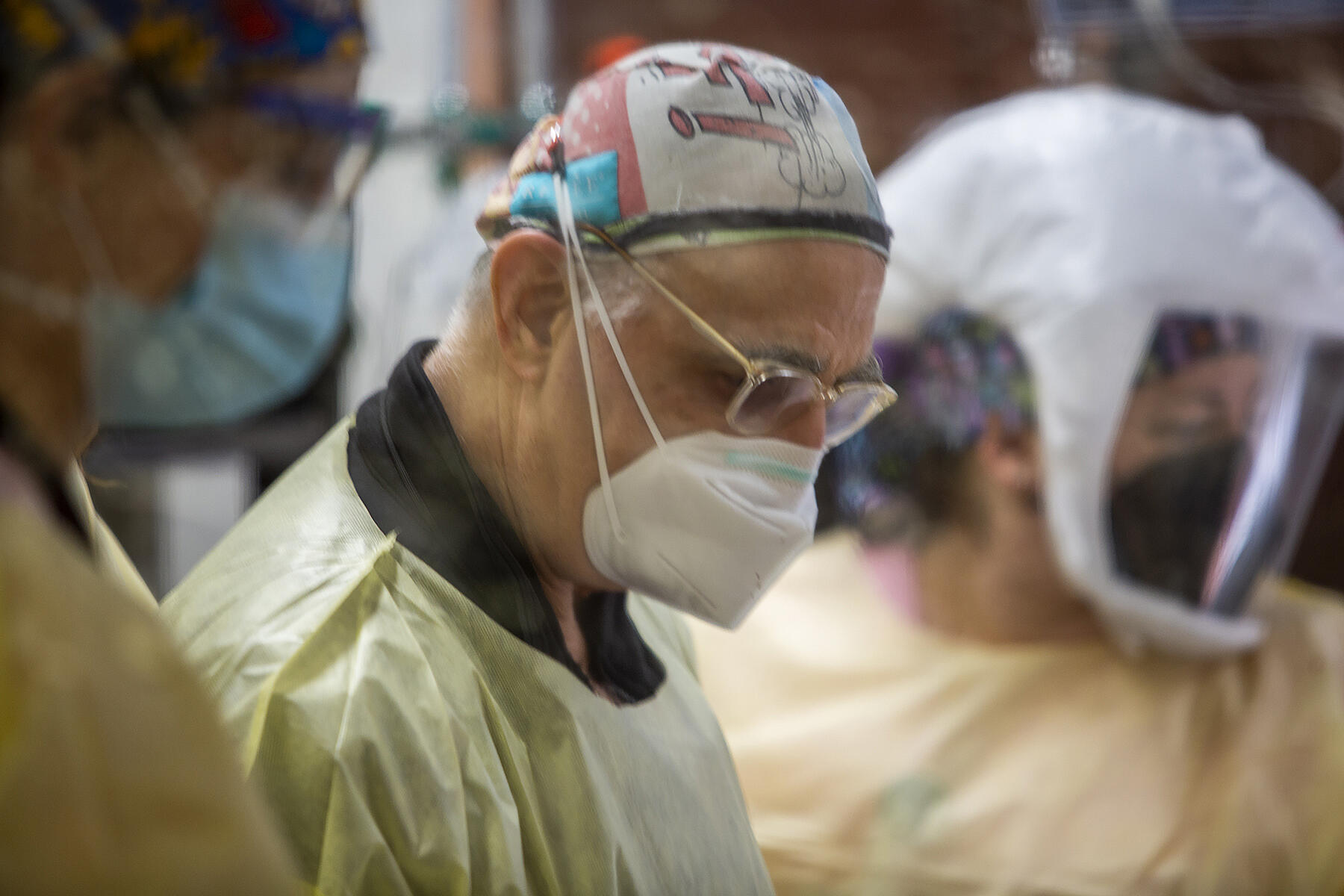 Three people in surgical masks and scrubs looking downward.