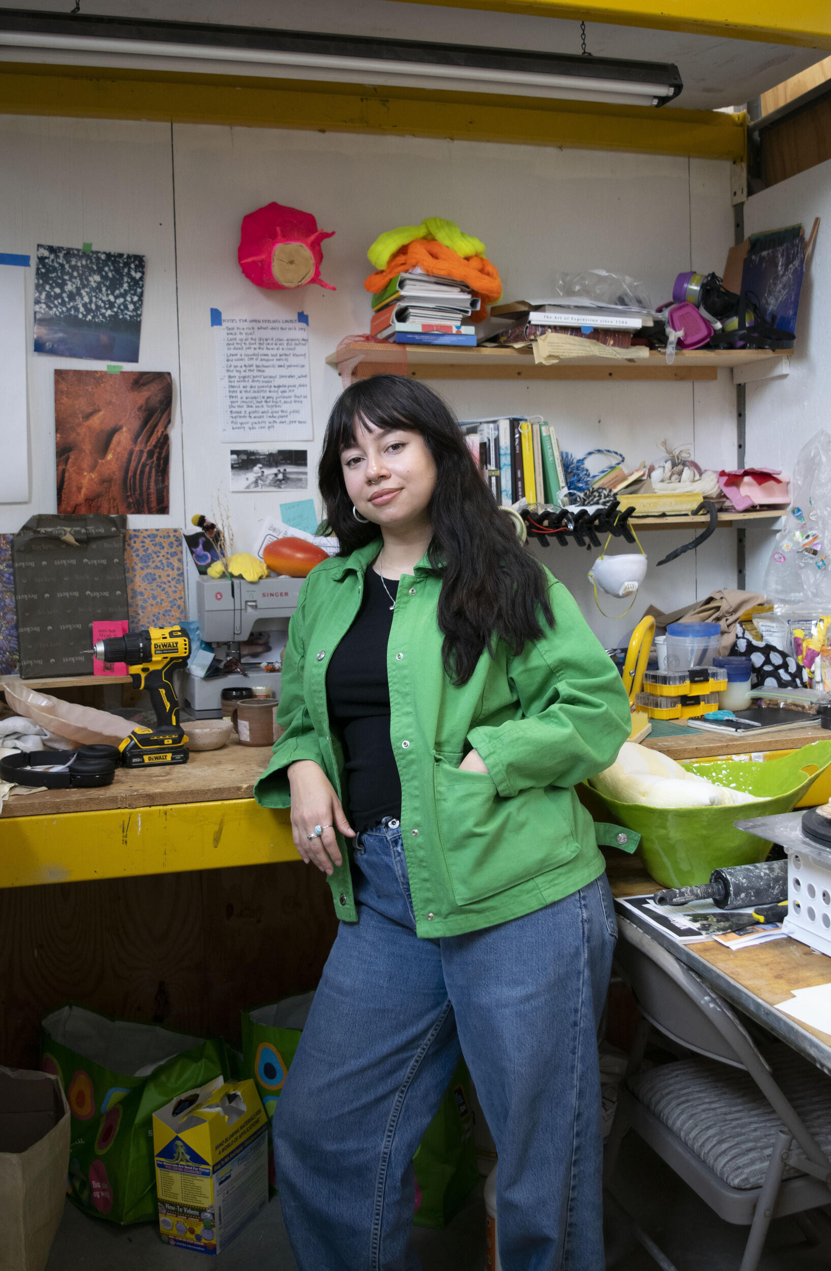 An image of a woman leaning against a desk in an art studio. 