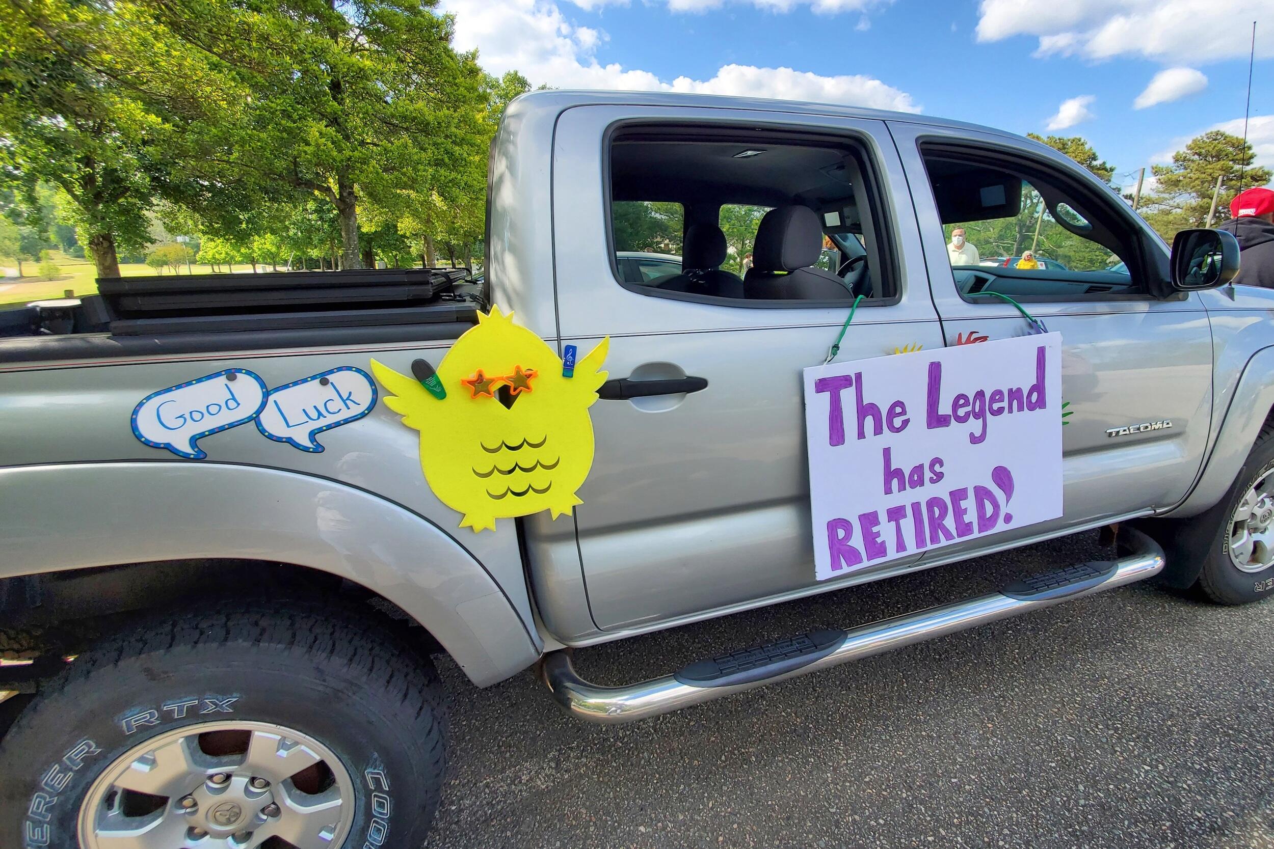 A passenger truck with two signs and a bird wearing star glasses hanging on its side.