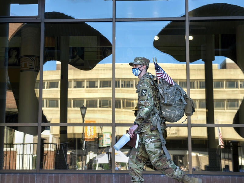 A photo of a man wearing a military uniform walking past a window with a reflection of ram horns on it. 