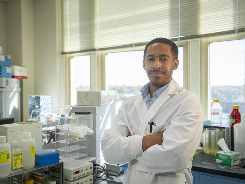 A photo of a man wearing a white lab coat standing with his arms crossed. 