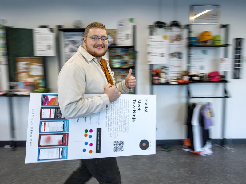 A photo of a man walking with a poster under his arm while giving a thumbs up 