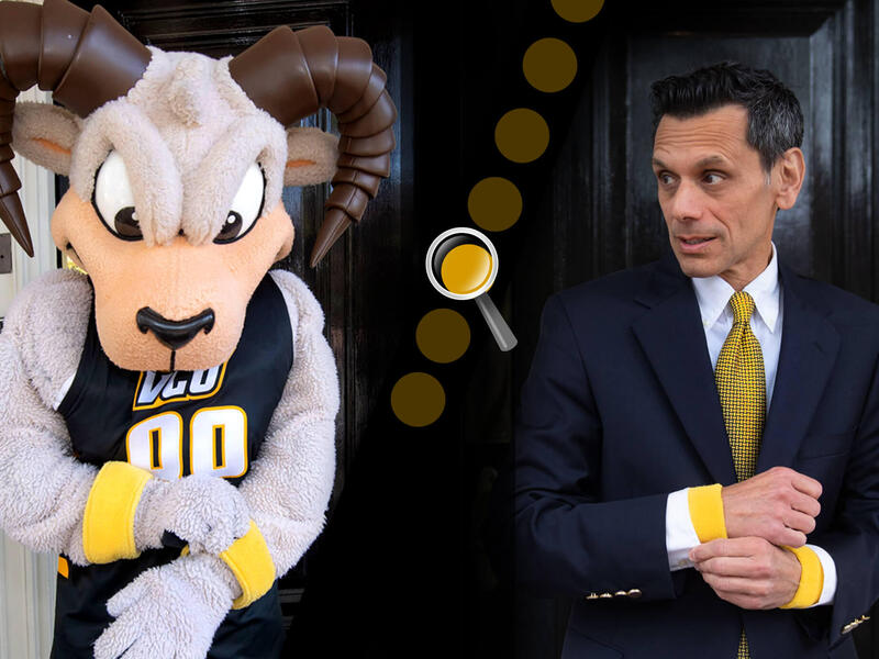 A man in a suit and tie standing to the right of a ram mascot costume. 