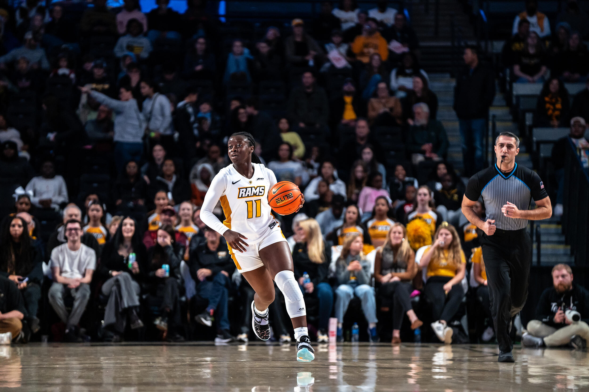 A photo of a woman playing basketball on a basketball court. Behind her is a crowd of people watching. 