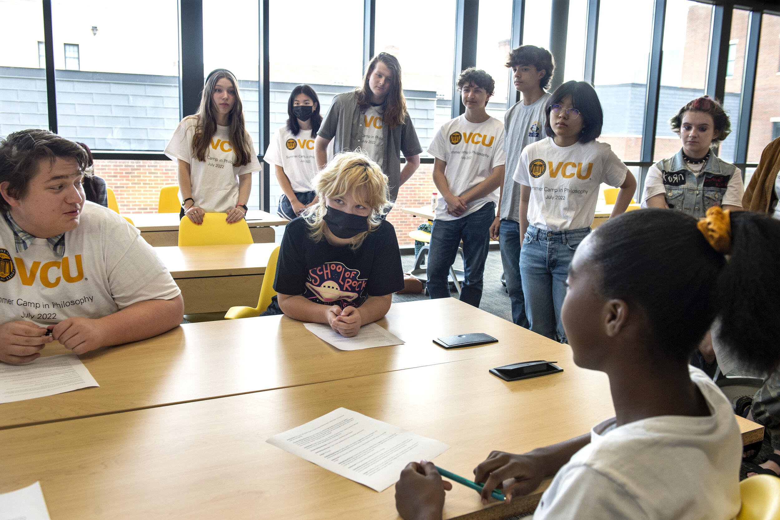 A photo of three people sitting at a table and a croup of people standing behind them. 