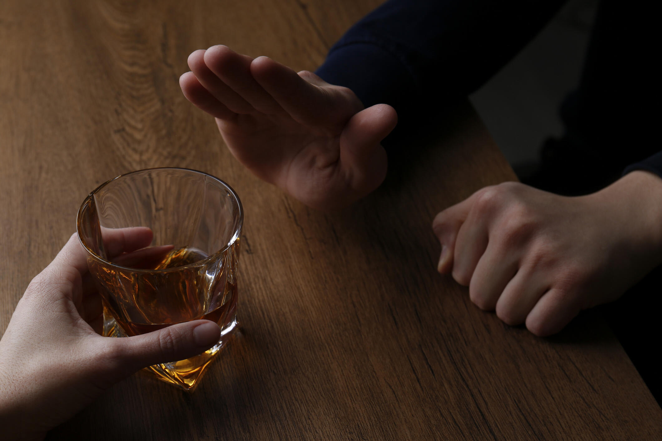 A hand on the left is holding a cup with brown liquid and a hand on the right is pointing upward in a \"stop\" gesture. 