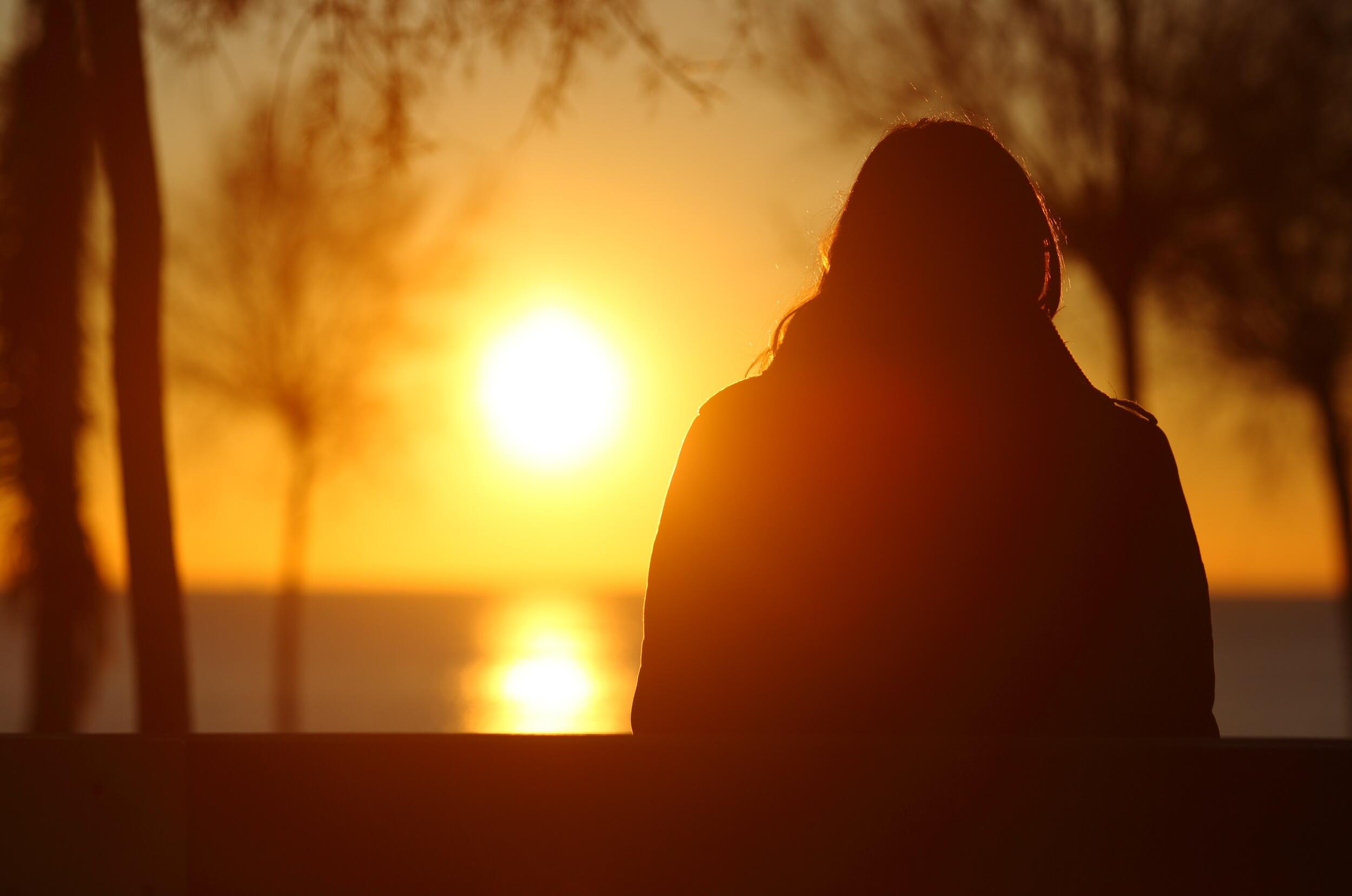 The silhouette of a person looking at the sun set over a lake 