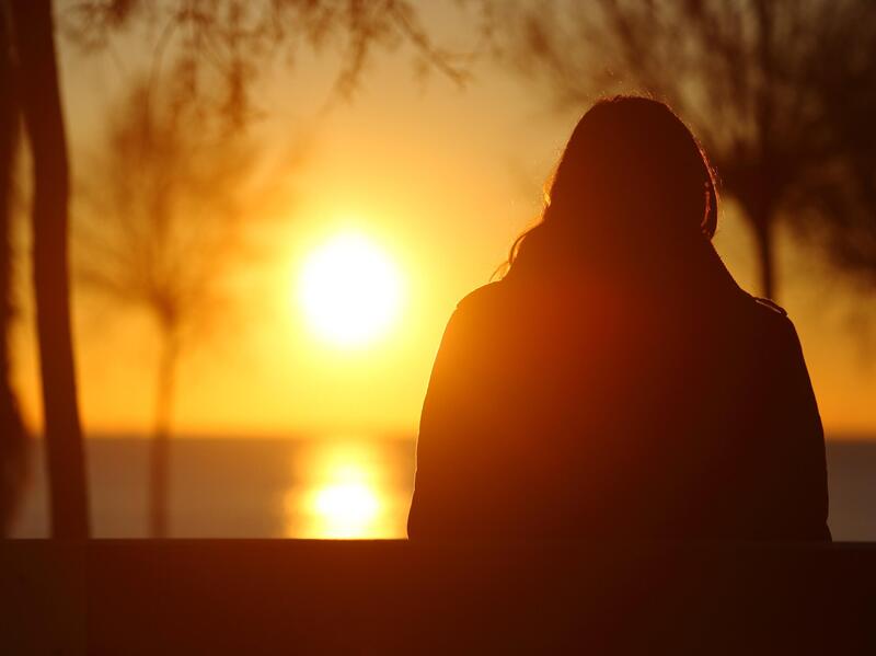 The silhouette of a person looking at the sun set over a lake 