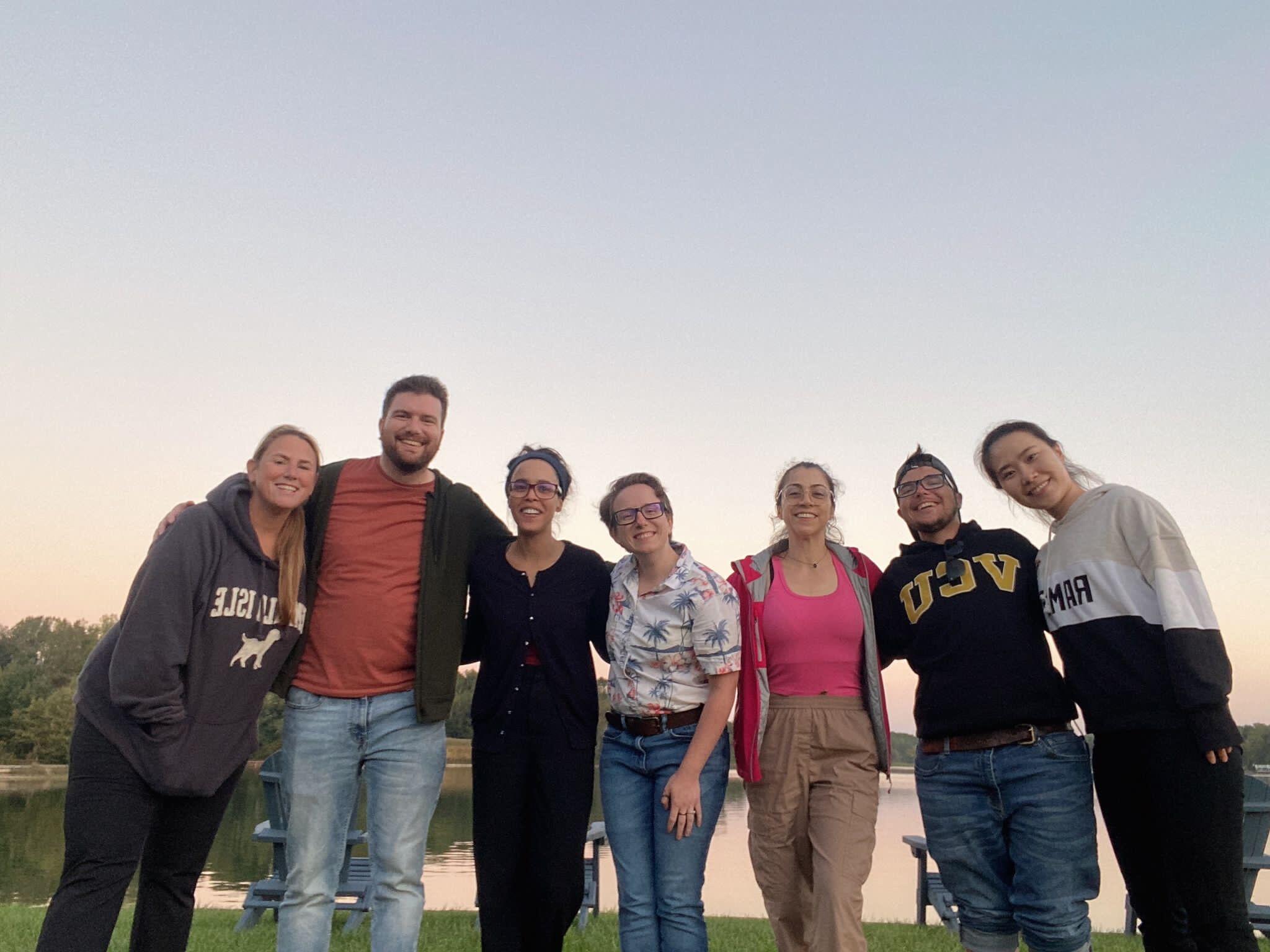 A group photo of seven people standing in front of a lake. 