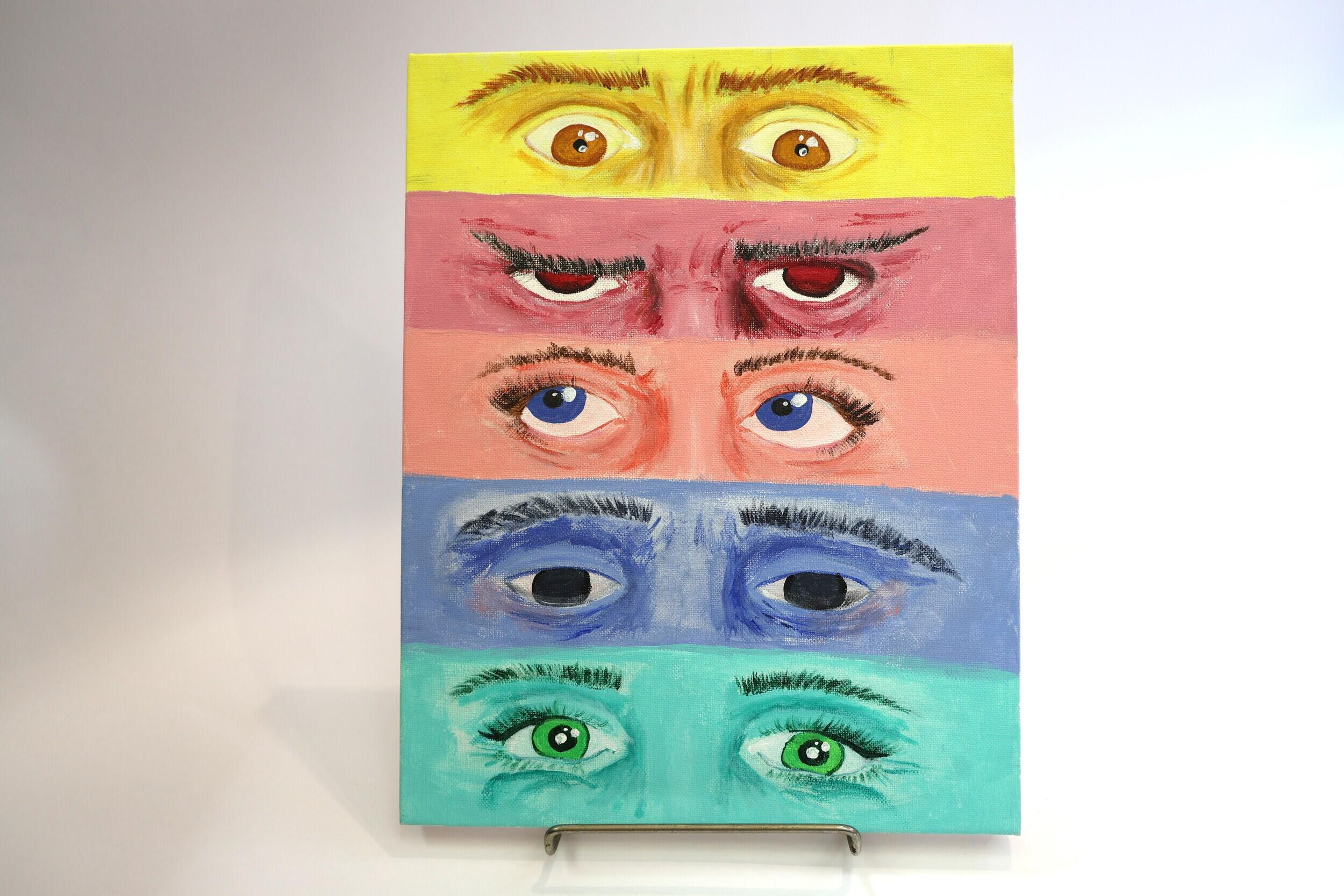 A photo of a canvas with five sets of eyes painted on it making different expressions. 