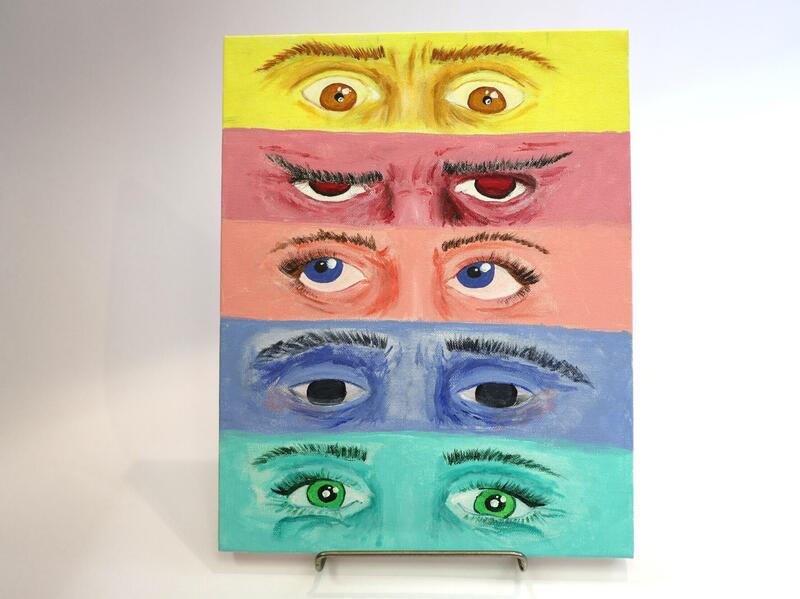 A photo of a canvas with five sets of eyes painted on it making different expressions. 