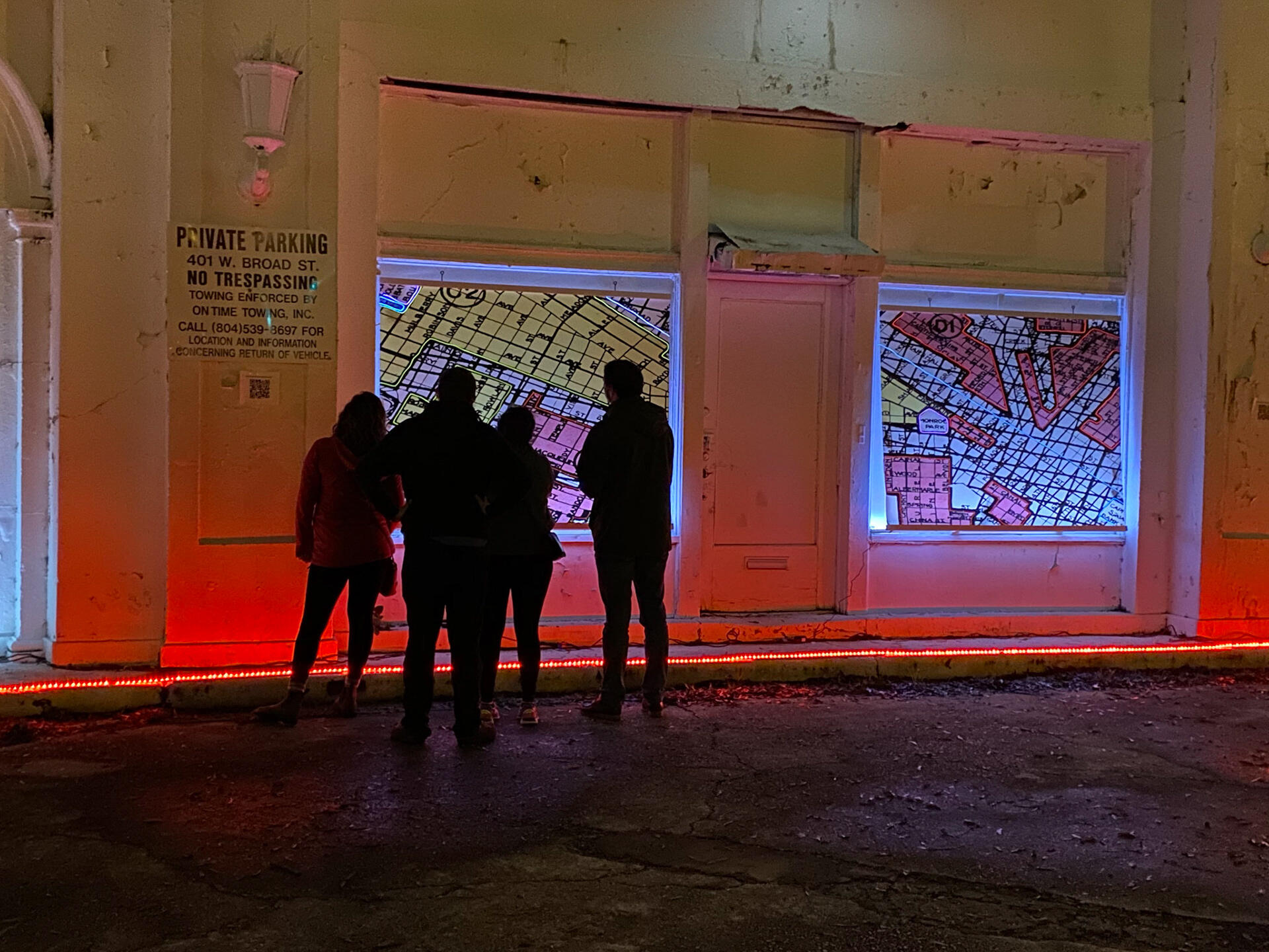 A photo of four people looking at an image illuminated on a wall. To the right of the image the people are looking at is a second one. 