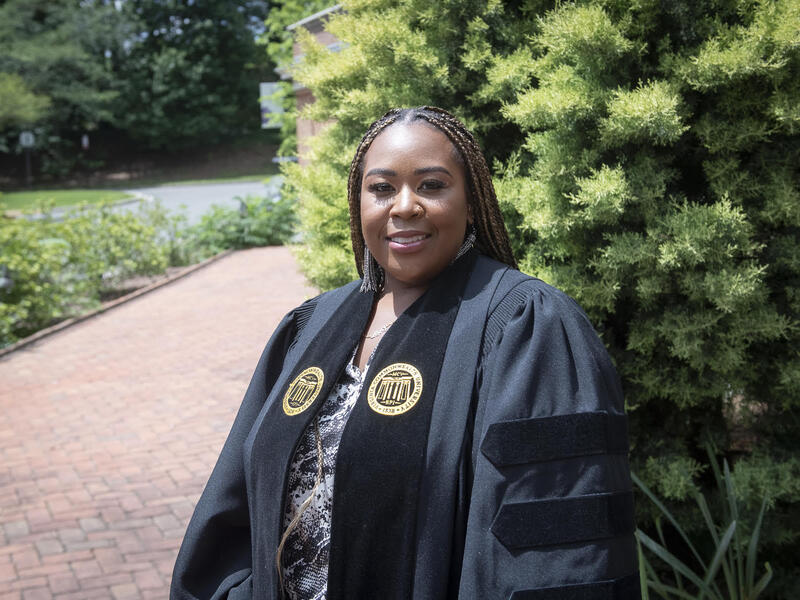 VCU graduate Briona Phillips, standing outside and wearing her graduation robe.