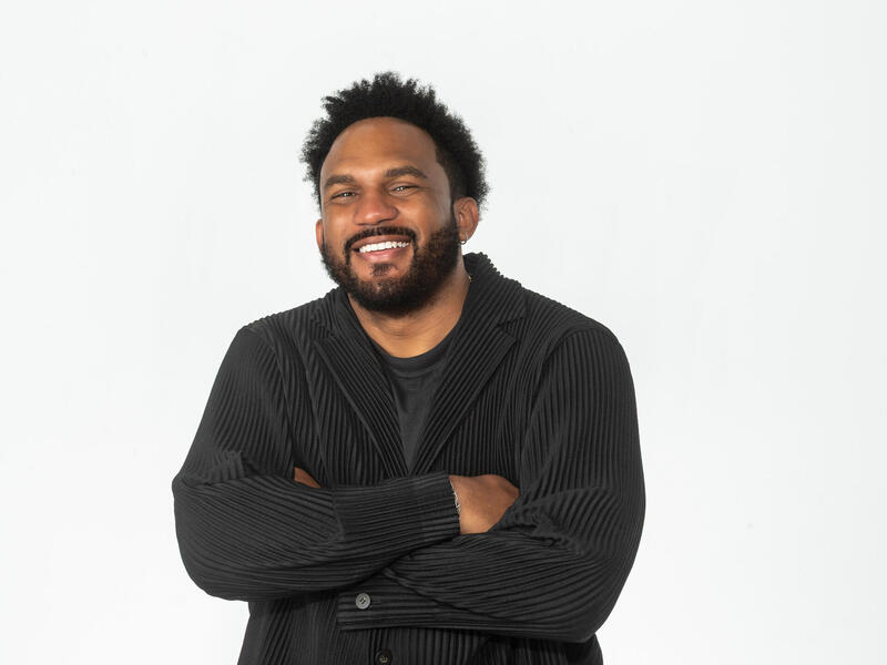 A photo of a man from the waist up. He is smiling and has his arms crossed against his chest. 
