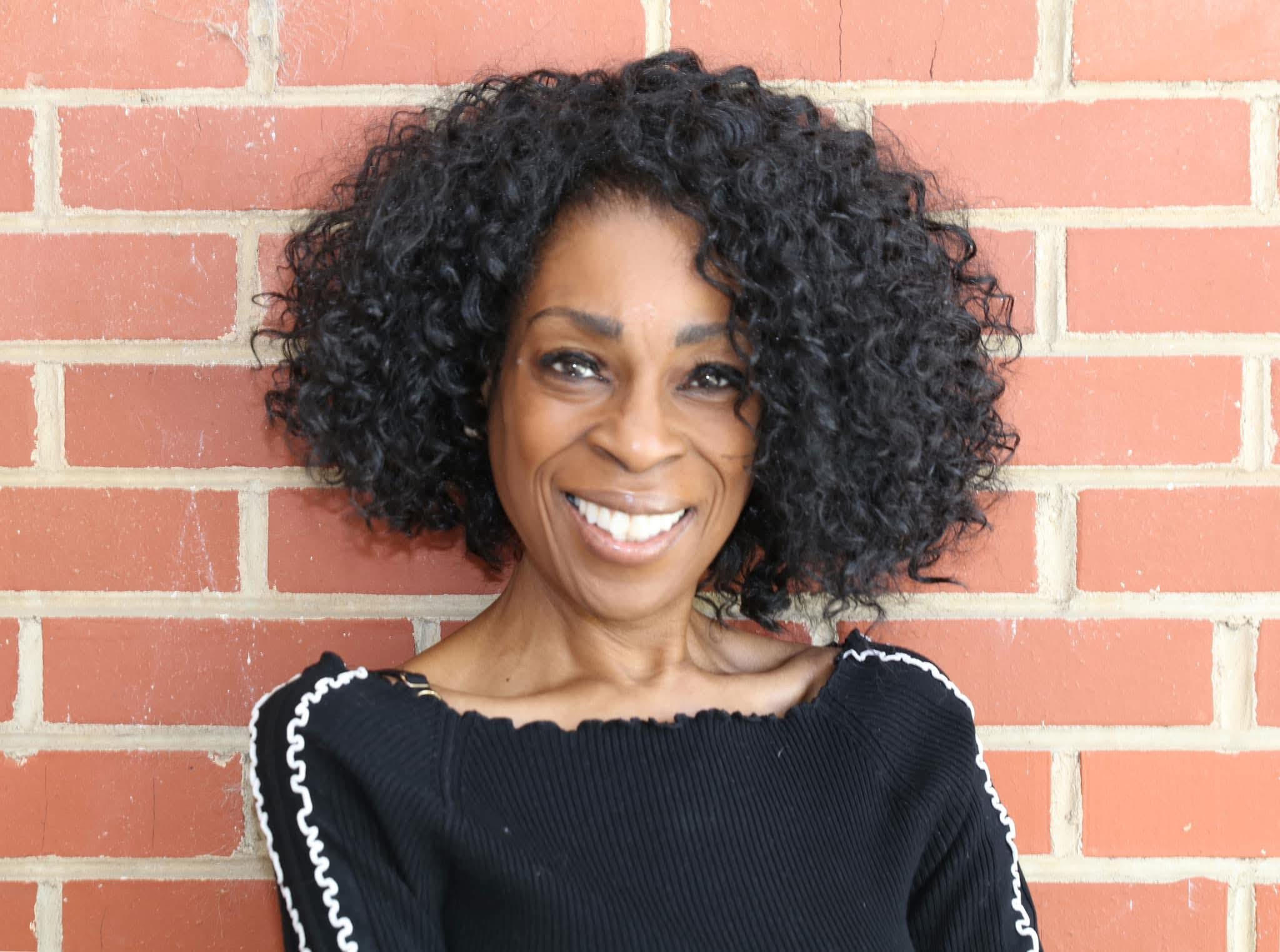 A woman in a black stop smiles in front of a brick wall.