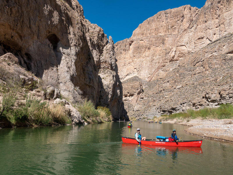 People in a red canoe on a river in the middle of two cliffs. 