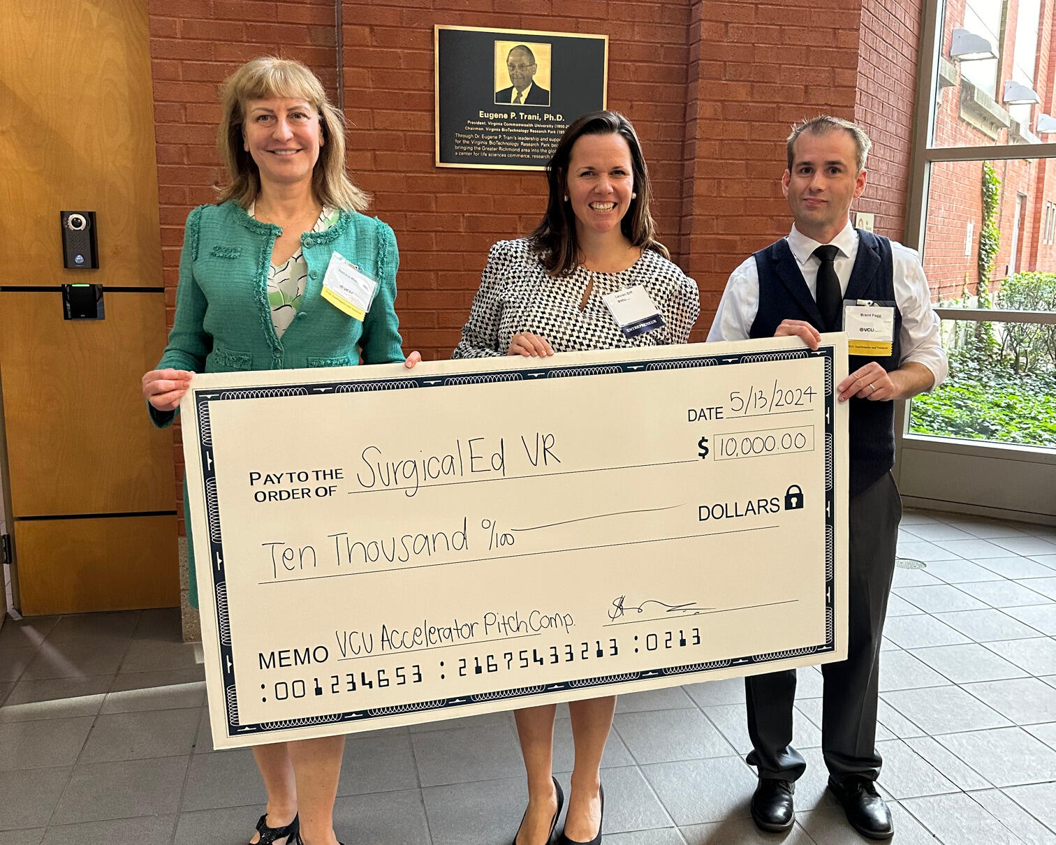 A photo of two women and a man holding a large check for ten thousand dollars. 