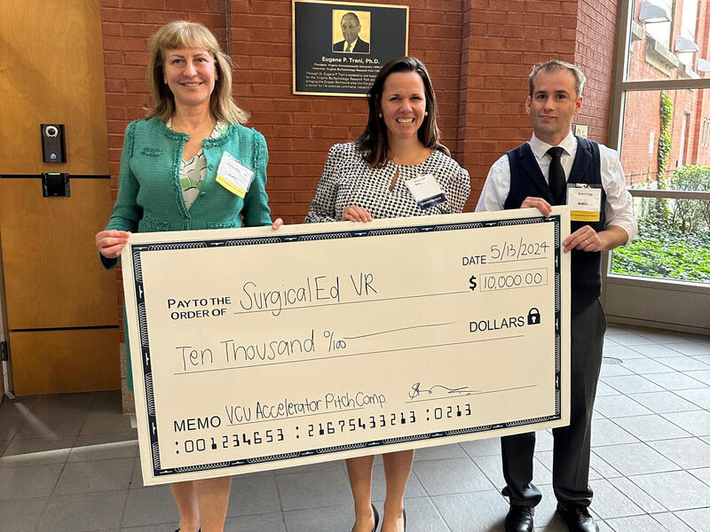 A photo of two women and a man holding a large check for ten thousand dollars. 