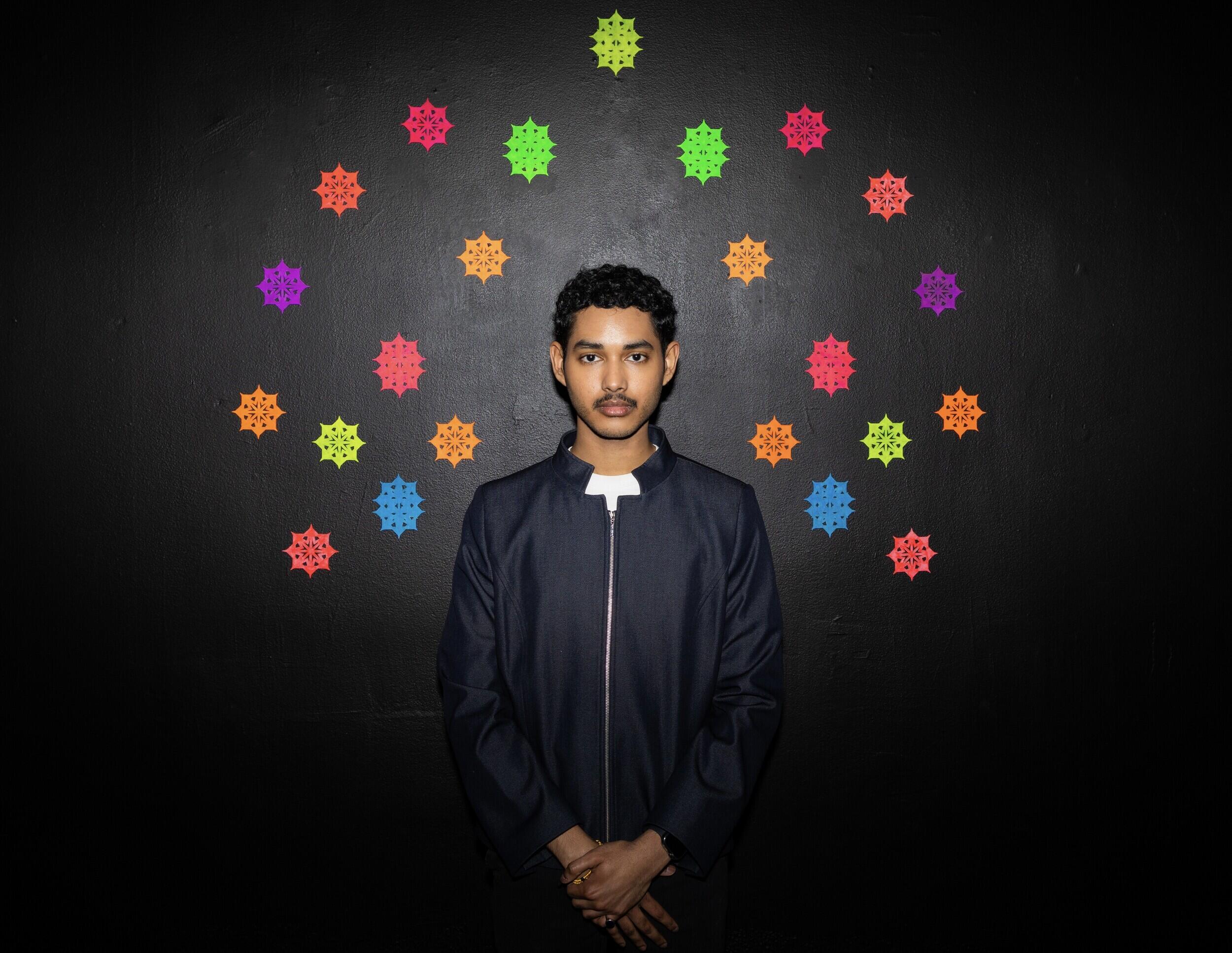 A photo of a man standing in front of a black wall. 