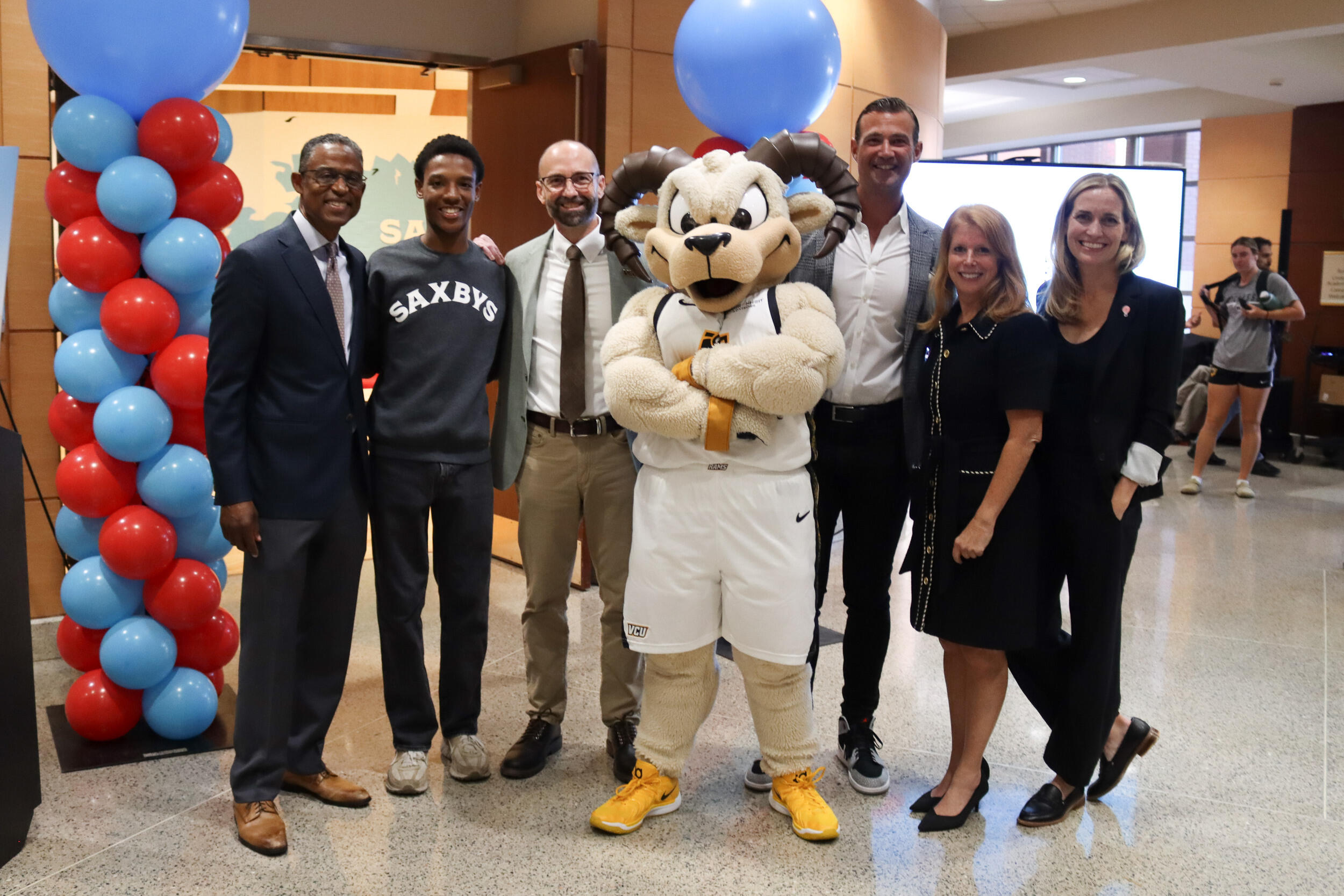 A photo of six people standing on either side of a person in a Rodney the Ram mascot uniform. 