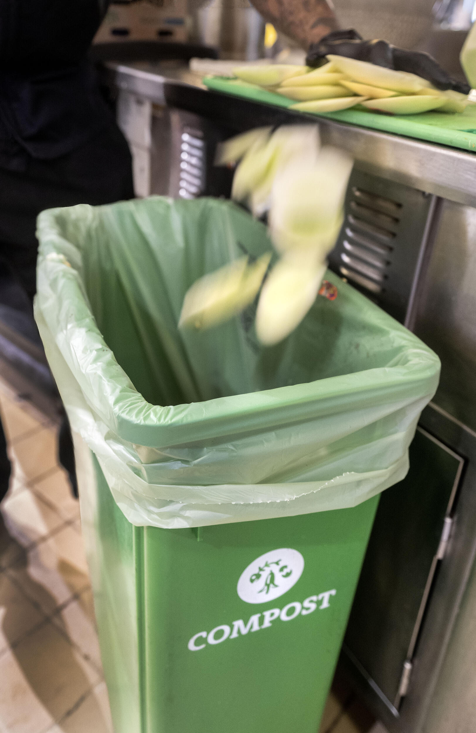 A photo of produce falling in a bin that says \"COMPOST\" 
