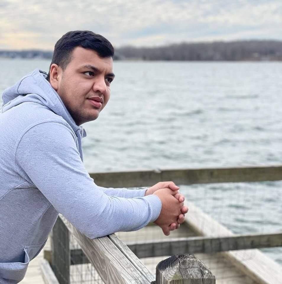 A man leans on a railing overlooking a body of a water.