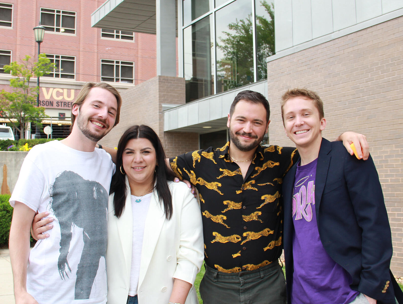 A photo of four people from the waist up who are standing outside. 