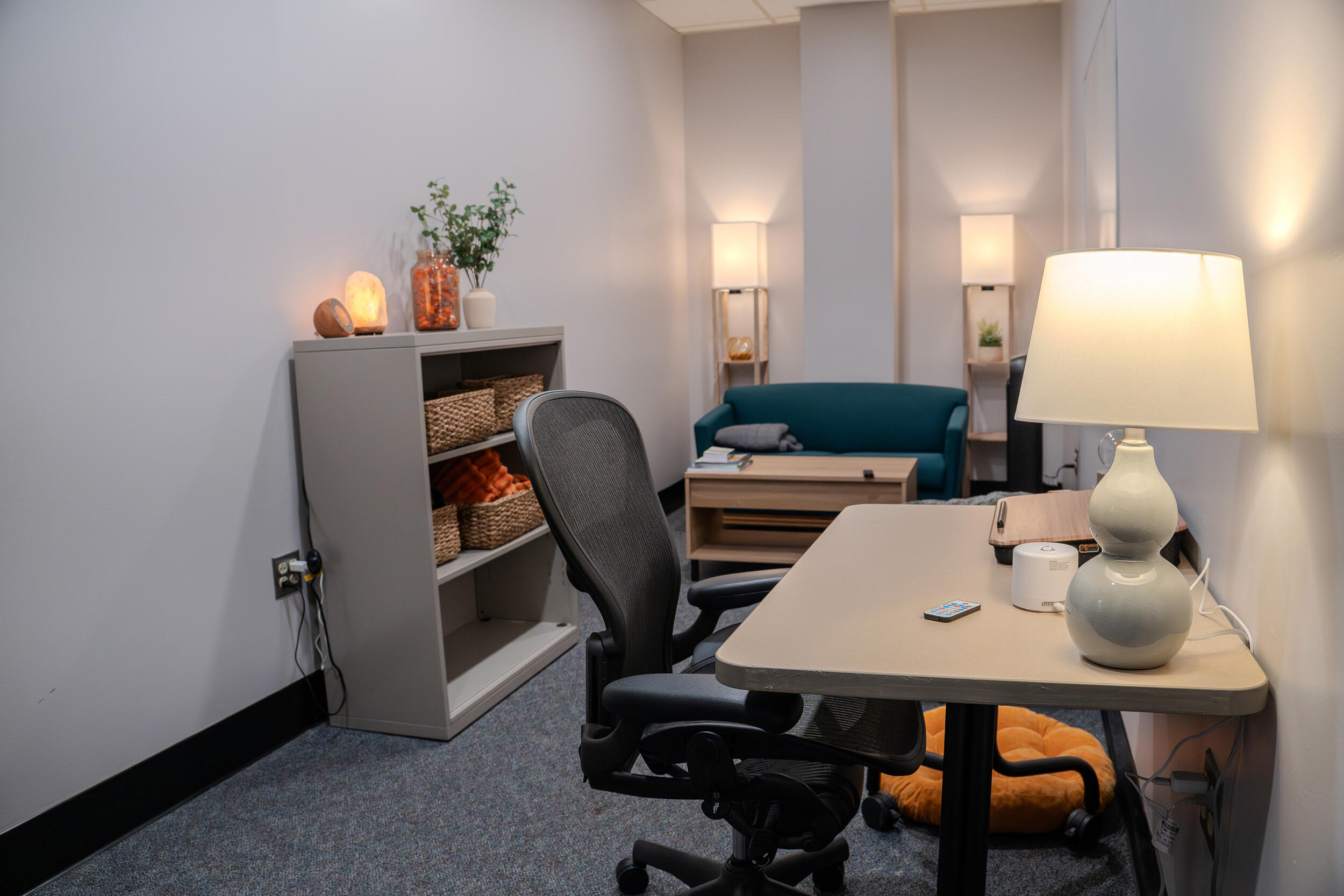 A photo of a room with a desk, chair, small book case, coffee table, and a couch.
