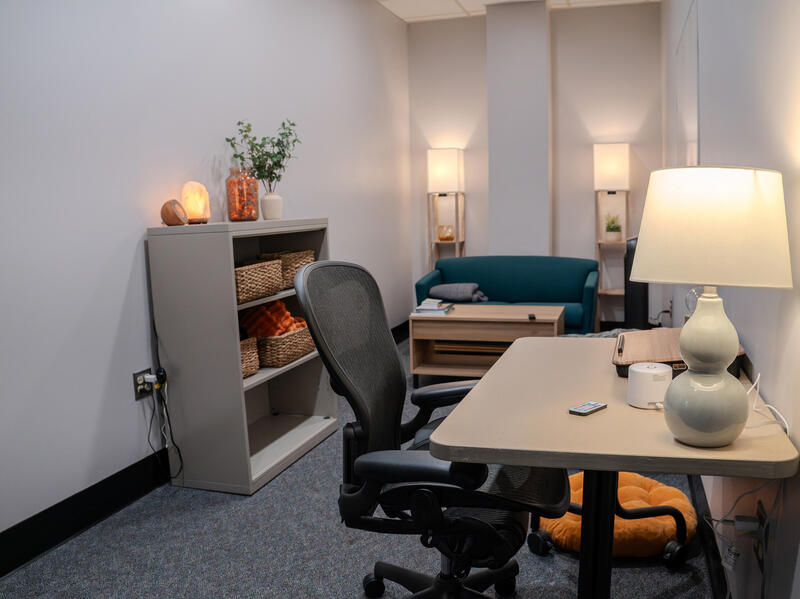 A photo of a room with a desk, chair, small book case, coffee table, and a couch.