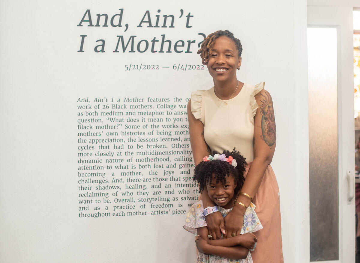 A woman standing behind a young girl, resting her hands on the girl's shoulders