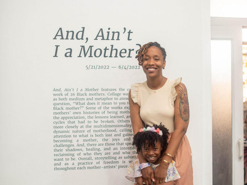 A woman standing behind a young girl, resting her hands on the girl's shoulders