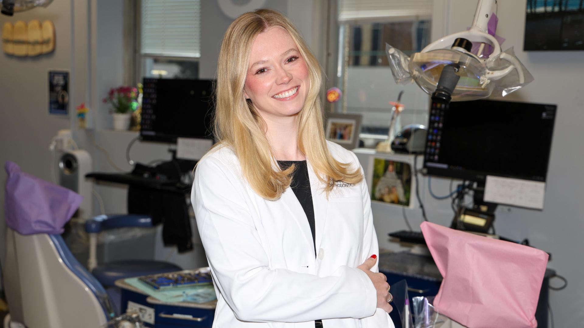 A photo of a woman wearing a white medical coat standing in a dental examination room.