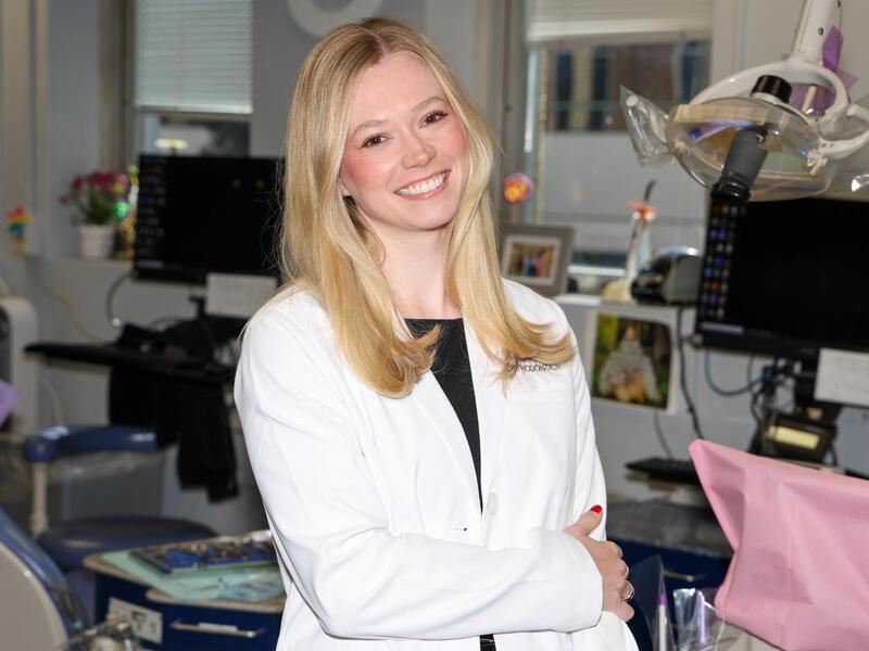A photo of a woman wearing a white medical coat standing in a dental examination room.