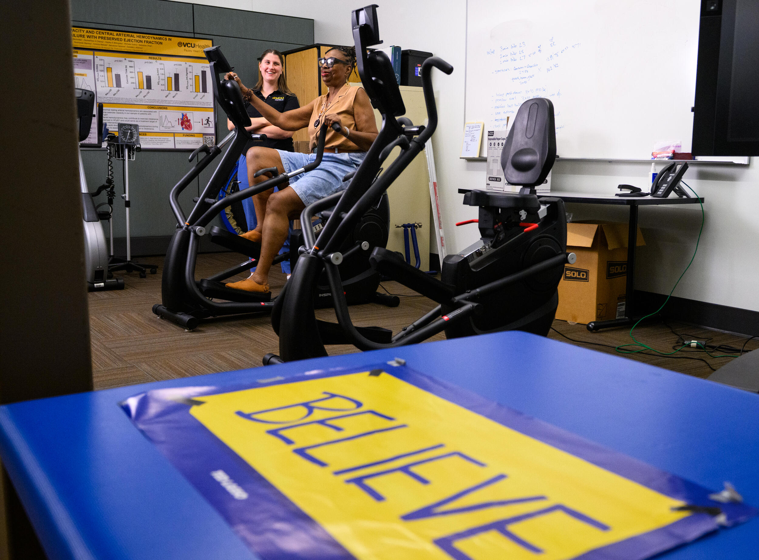 A photo of a woman on an exercise bike with another woman standing next to her. 
