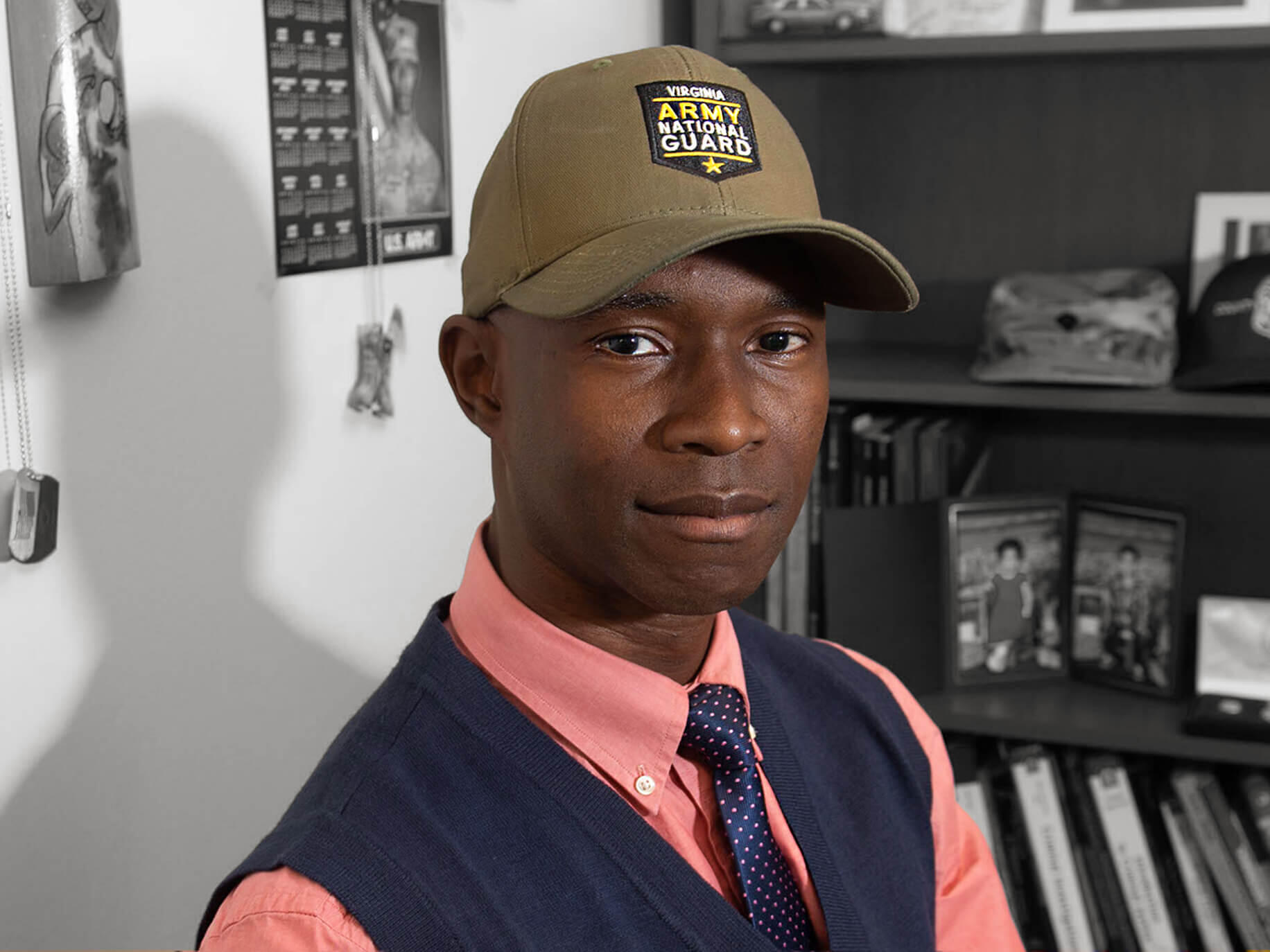 A man wearing a vest, tie, and baseball hat looking at the camera. 