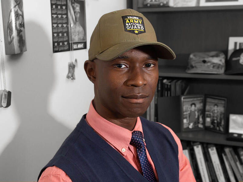 A man wearing a vest, tie, and baseball hat looking at the camera. 