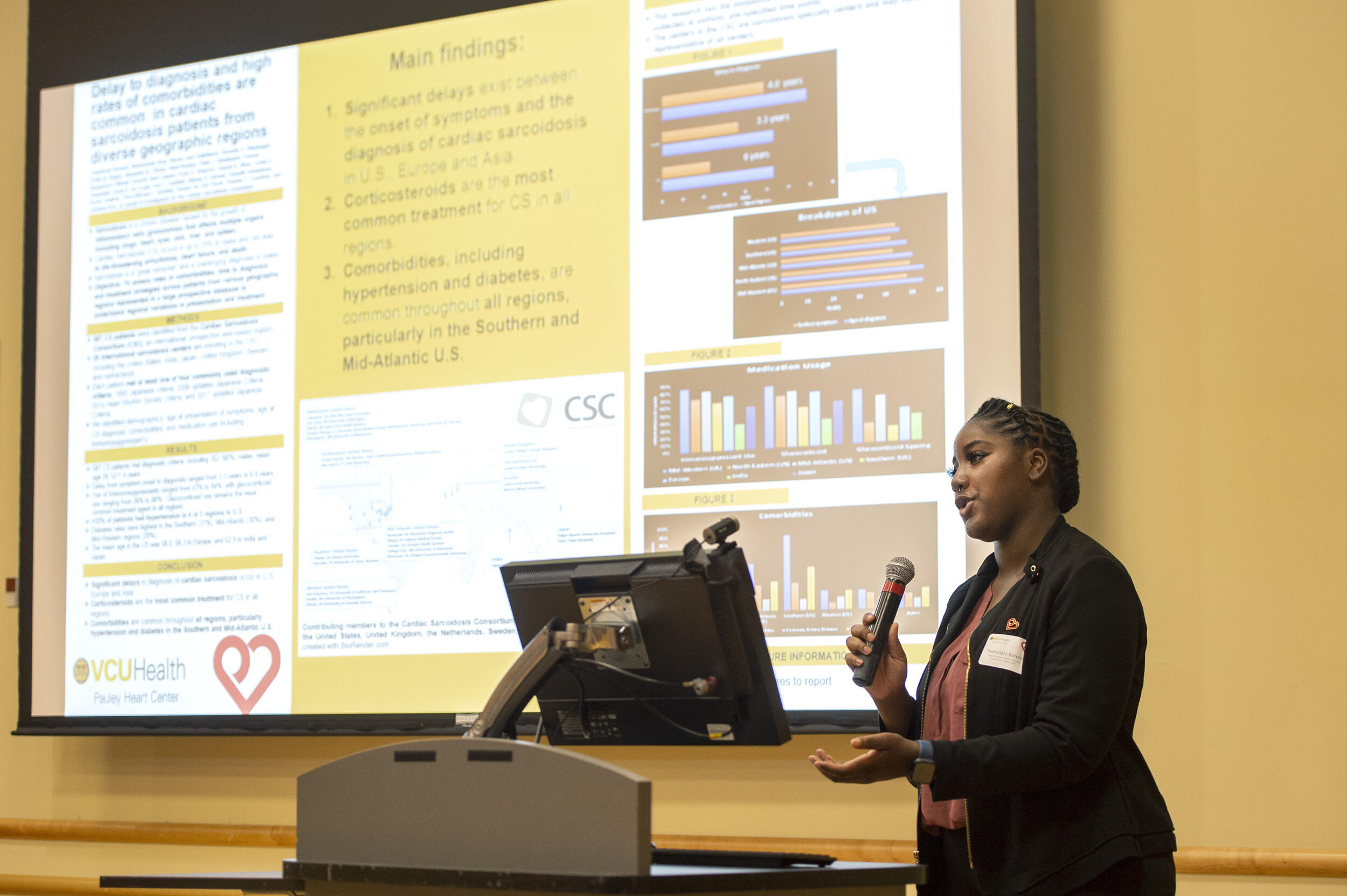 A woman speaking into a microphone next to a presentation she's giving 