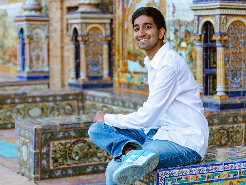 A man wearing a white long sleeve shirt and blue jeans sitting on a mosaic tile cube 