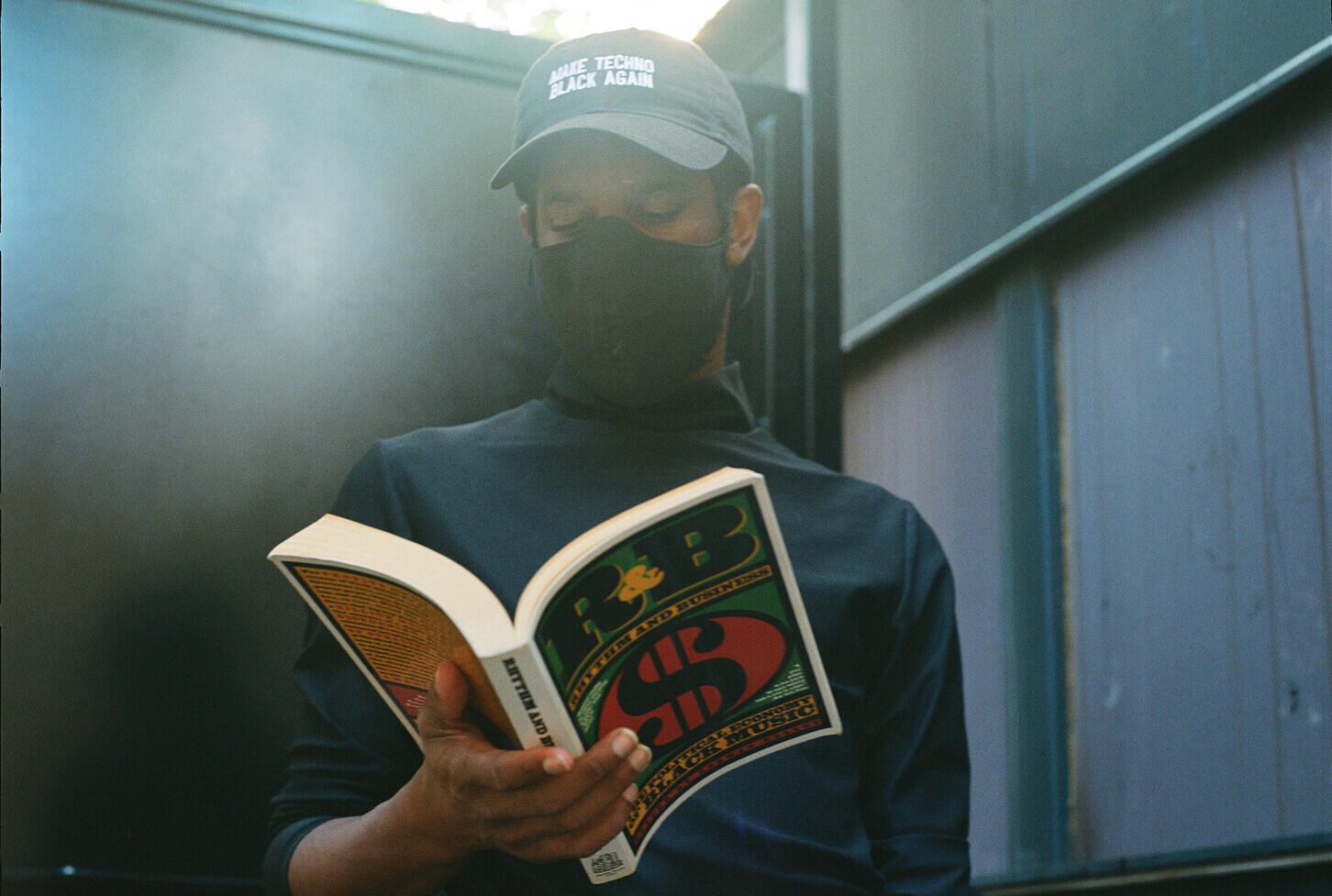 DeForrest Brown Jr reading a book while wearing a baseball cap and black face covering
